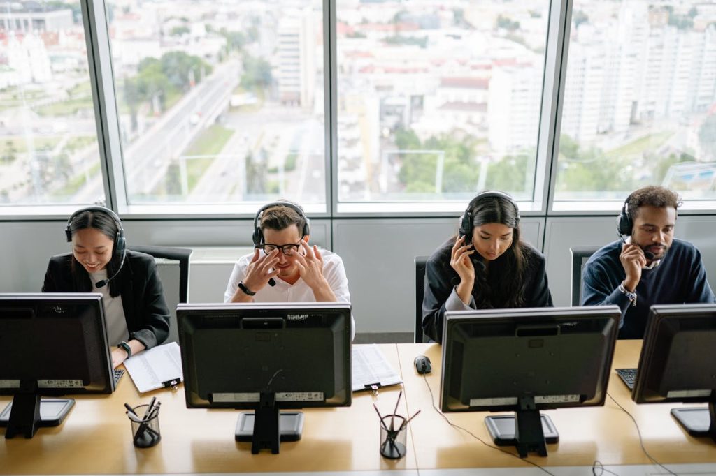 Group of diverse call center employees working at computers in a modern office setting.